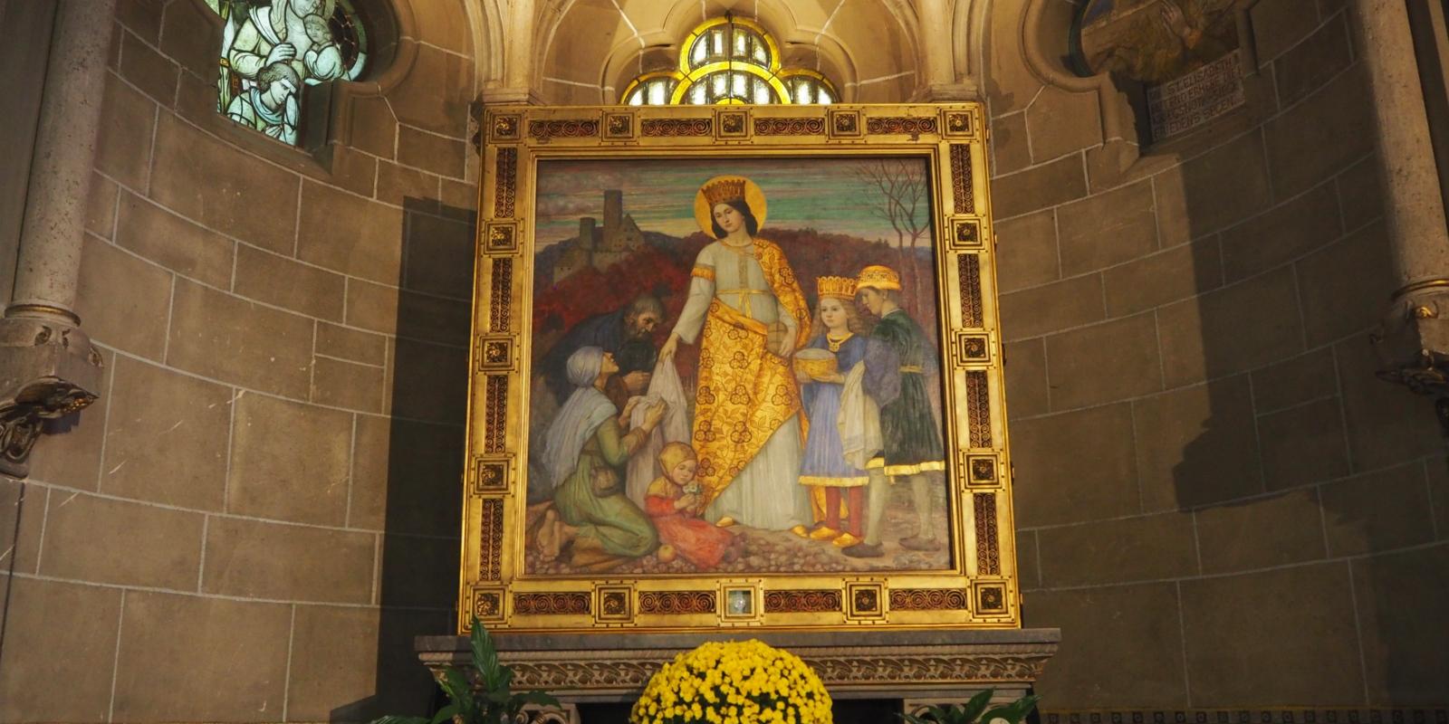 Elisabeth-Altar von Matthäus Schiestl. Der Elisabeth-Altar im nördlichen Seitenchor entstand 1915.  Er zeigt die Markgräfin von Thüringen Elisabeth, wie sie mit ihren beiden Kindern Brot und Kleidung an die Armen verteilt.  Elisabeth von Thüringen (* 1207[1] in Pressburg oder auf Burg Rákóczi in Sárospatak (Ungarn); † 17. November 1231 in Marburg an der Lahn), auch Elisabeth von Ungarn genannt, war eine ungarische Prinzessin, deutsche Landgräfin, ist Heilige der katholischen Kirche und galt als „deutsche Nationalheilige“. Ex-Bild-DB-ID: 27078